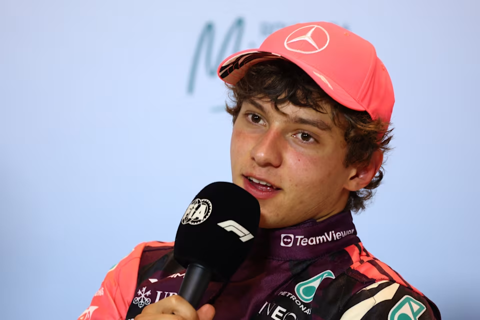 Kimi Antonelli respondendo perguntas na entrevista coletiva com o novo kit da Mercedes de macacão rosa, preto, branco e magenta escuro em estampa floral, e boné rosa com a mesma estampa na parte interna.