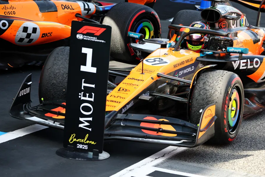 Uma imagem de um carro de Fórmula 1, mais especificamente da equipe McLaren, na pista de corrida de Barcelona, com a numeração "1", devido ao primeiro lugar conquistado ao final, e os patrocinadores, como Moët, visíveis no carro e em um painel à frente.